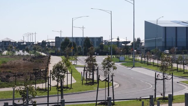 a newly constructed suburban road lined with staked young saplings, modern housing, and a public school facility in&nbsp;Truganina, Melbourne, Australia. Master-Planned Community Development