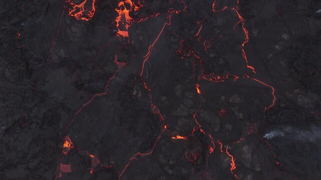 Aerial view of glowing molten lava flowing through dark volcanic rock fissures in Reykjavik, Reykjavikurborg, Iceland.