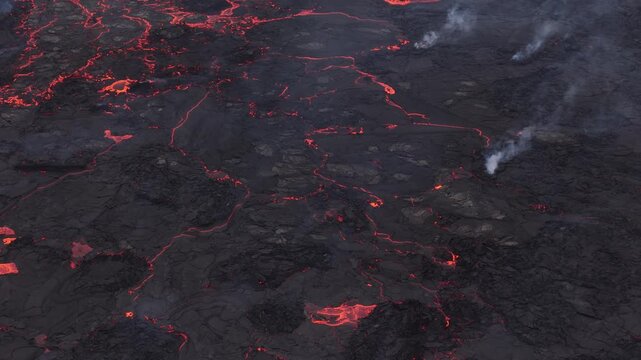 Aerial view of glowing lava flowing through dark volcanic terrain with plumes of smoke rising from the cooling crust Reykjavik, Reykjavikurborg, Iceland.