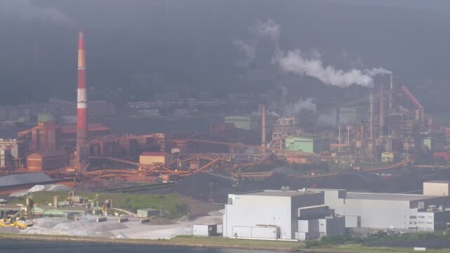 煙突から煙を上げる工場がある港の風景。