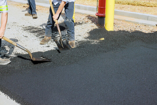 Two workers use shovels to spread asphalt on ground next to fire hydrant