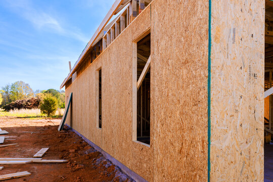 Workers are building wooden structure outdoors installing plywood OSB panels with open windows