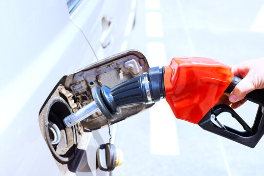 Person holds fuel nozzle while filling car tank with gasoline at gas station.