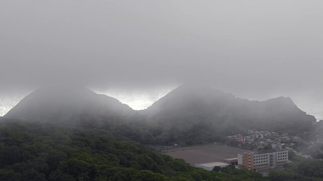 流れる雲の中だら山と街を望む風景。