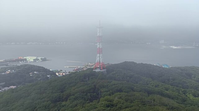 流れる雲の先に電波塔がたつ山が見える風景。
