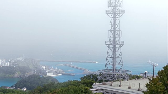 雲の中からアンテナ塔と漁港を望む風景。