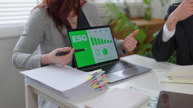 Businesswoman presenting ESG environmental and social governance data to a colleague on a green screen laptop during a meeting