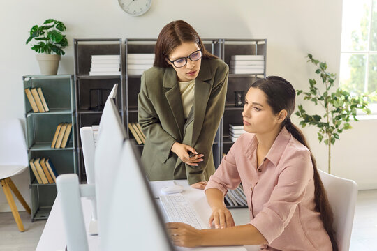 Women analysts collaborate at a computer workstation. One guides as the other types, focusing on analytics reporting and data strategy. Clear mentoring teamwork concept for business today.