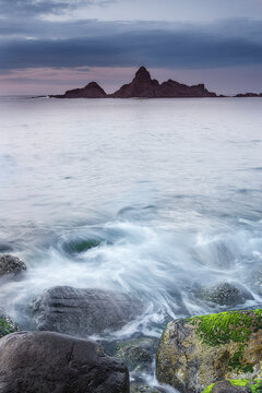 Beautiful sunset at Saturraran beach with colorful dramatic clouds purple horizon rocky sea stack and long exposure ocean waves crashing on mossy rocks