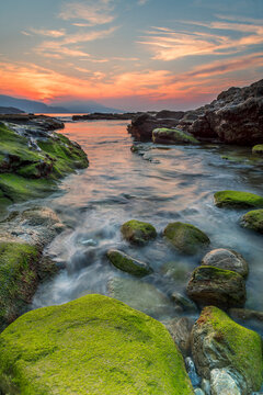 Golden sunset over rocky coast with vibrant green moss tide pools and dramatic sky at Lastron beach in Zierbena
