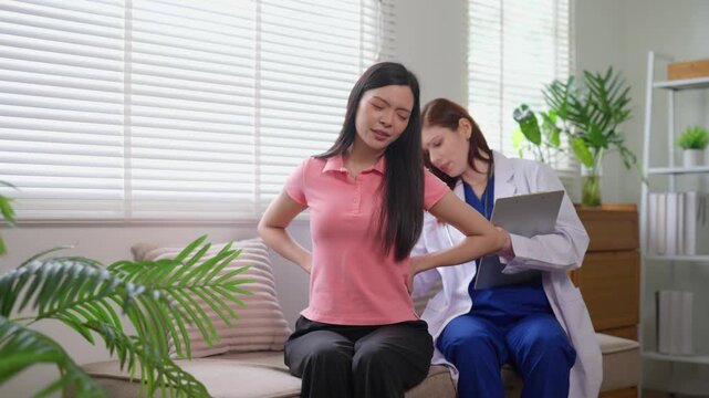 Female doctor examining asian patient with back pain during medical consultation in clinic. Woman feeling discomfort in lower back