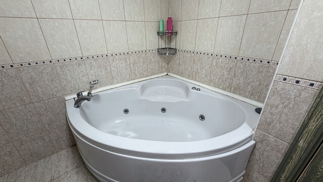 White corner whirlpool bathtub with massage jets in a tiled residential bathroom interior.
