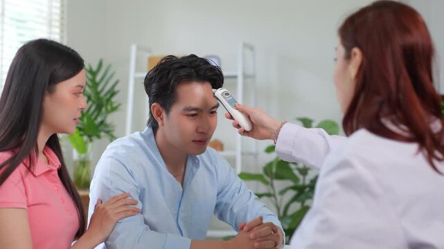 Doctor checking man's temperature with an infrared thermometer while his wife provides support in a medical clinic