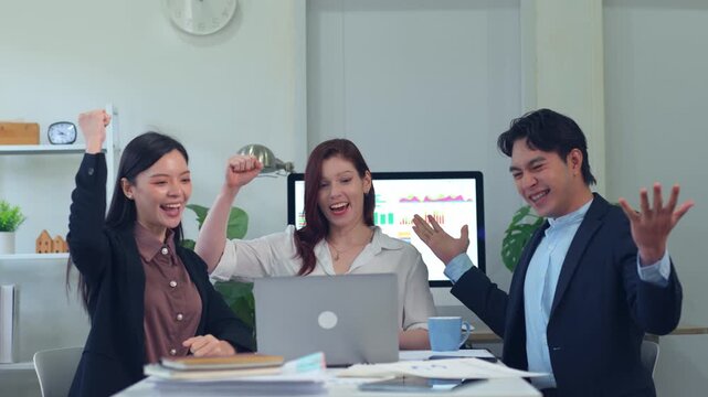 Excited business team celebrating success with a laptop and raising their fists in the office while looking at financial charts