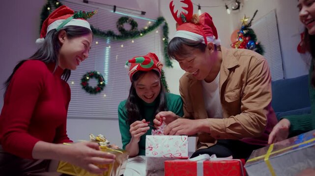 Happy asian friends unwrapping gifts together during a festive christmas party at home and laughing
