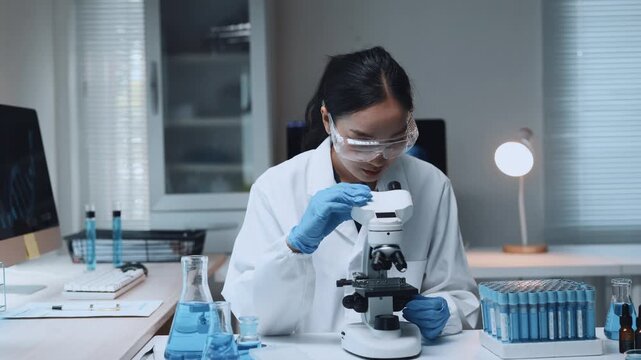 Asian female scientist developing vaccine in laboratory using microscope for medical research and pharmaceutical development