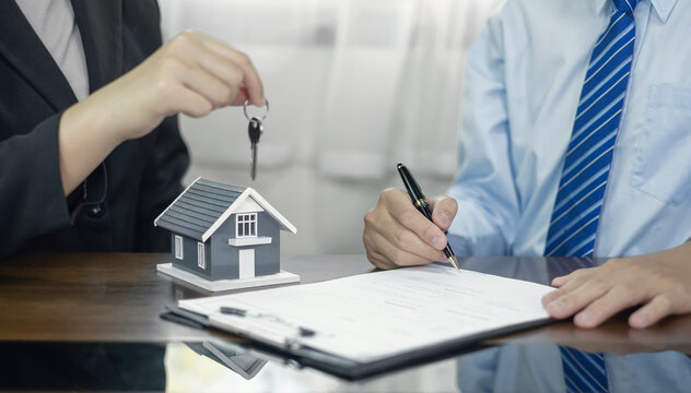 Real estate agent giving key to client signing agreement contract with house model on desk for home loan mortgage purchase and property insurance concept