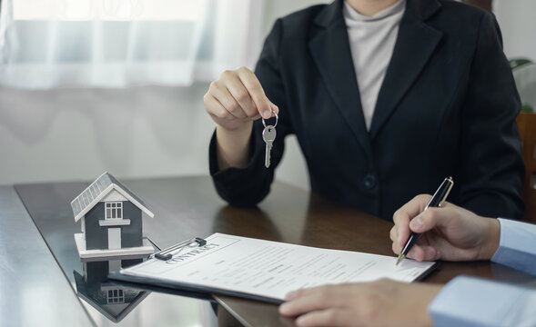 Real estate agent giving key to client signing agreement contract with house model on desk for home loan mortgage purchase and property insurance concept