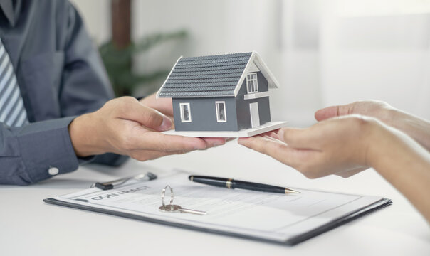 Real estate agent giving house model to client with contract and key on desk for home loan mortgage approval and property insurance concept