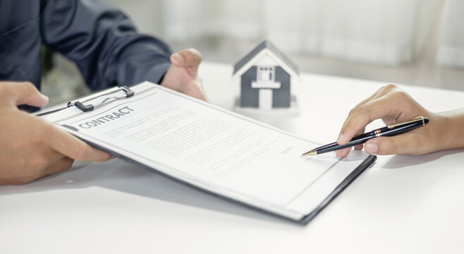 Real estate agent submitting agreement contract for client signing with house model on desk for home loan mortgage purchase and property insurance concept