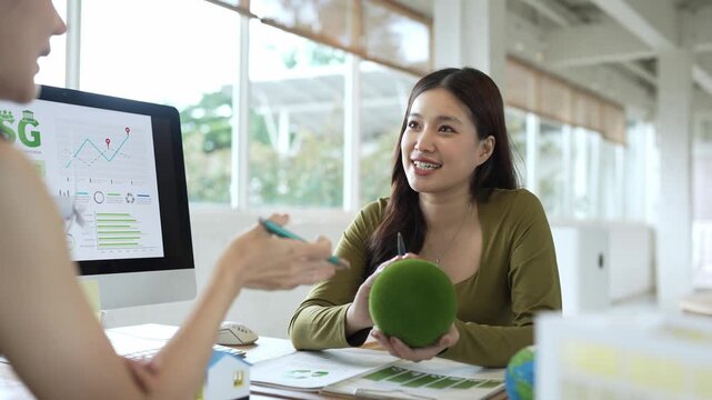 Asian architect discussing green building design and sustainable ESG strategy with a colleague in a modern office meeting
