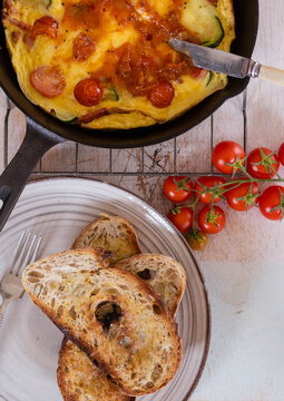 Golden omelette in cast-iron skillet with two slices of artisan toasted bread on the side