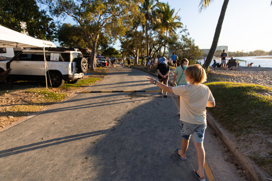 Two young people walk along a sunlit path near a beachside