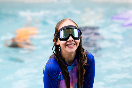 Young girl standing in a swimming pool wearing a rash guard and large reflective goggles