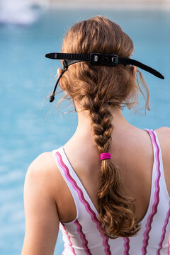 Young girl with long braided hair in pink striped swimsuit standing at the poolside