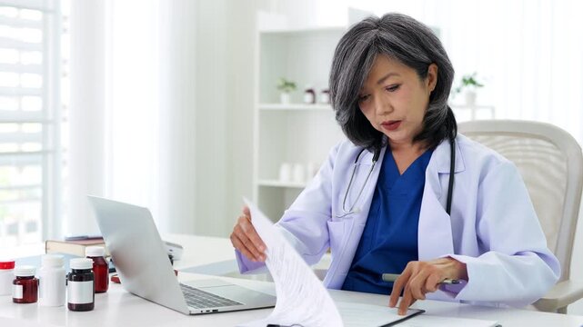 Stressed Female doctor nurse sit by laptop computer while reviewing patient medical charts at the clinic office.