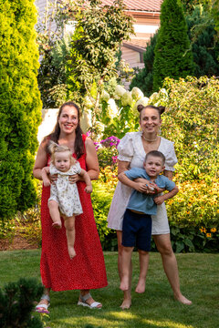 Smiling Women Holding Children in Lush Summer Garden