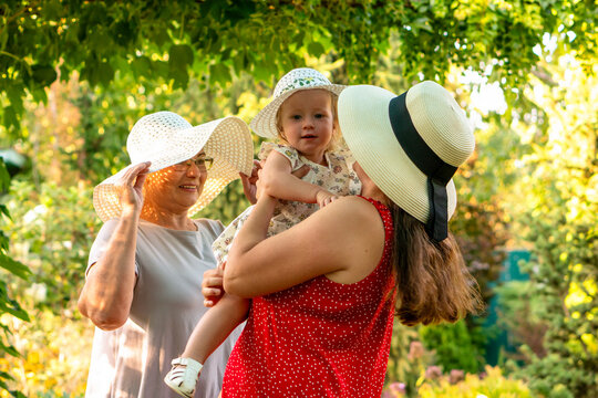 Three Generations Wearing Sun Hats In Summer Garden