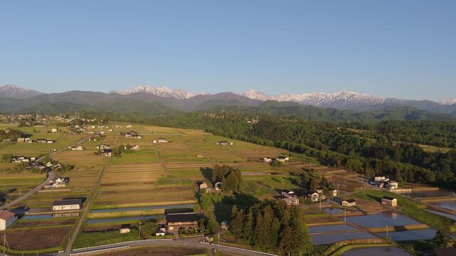 Aerial panorama of rural farmland and village beneath snow-capped mountains