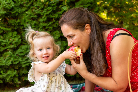 Smiling Daughter Sharing Bitten Apple With Mother Outdoors