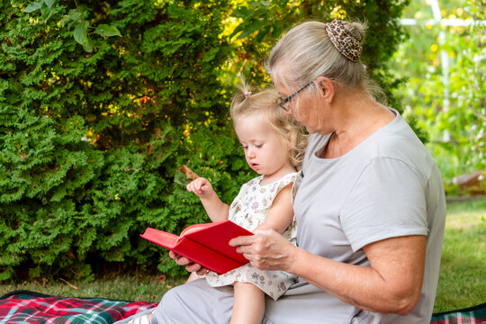 Young Granddaughter Exploring Book With Grandmother Outdoors in Garden