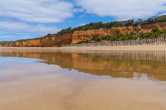 Golden sandstone cliffs reflecting across calm beach at low tide shoreline