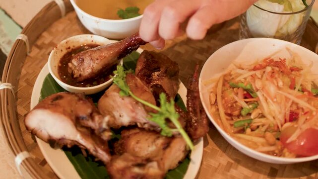 Hand Dipping Grilled Chicken into Sauce with Papaya Salad