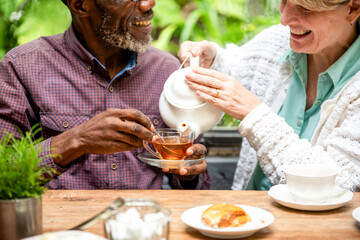 Two people enjoying tea together at an outdoor table with pastries.