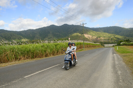 Young couple riding a scooter on a Queensland road with sugarcane fields