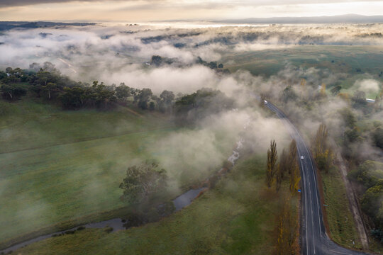 Winding country road cutting through a fog‑covered rural landscape