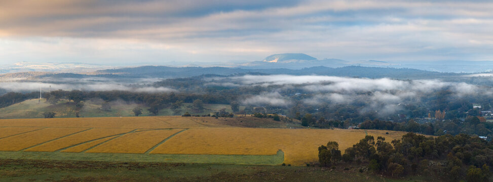 Morning mist lingering above golden farmland beneath distant mountain ranges