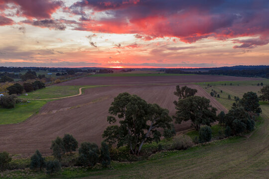 Fiery sunset glowing above peaceful farmland beneath colourful evening clouds