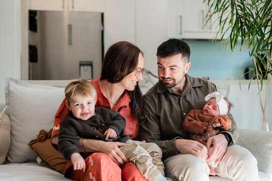 A couple sits on a sofa with their two young children, enjoying each other's company in a home