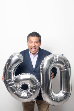 60-year-old Latino man with a dark skin displays 60 shaped balloons to celebrate his birthday and his entry into his old age