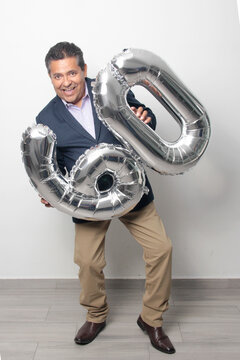 60-year-old Latino man with a dark skin displays 60 shaped balloons to celebrate his birthday and his entry into his old age