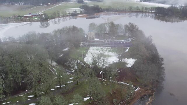 Aerial drone shot showing Grafsnas Castle Park surrounded by flooded fields, trees, water and historic buildings near Lake Anten in Alingsas, Sweden during winter weather