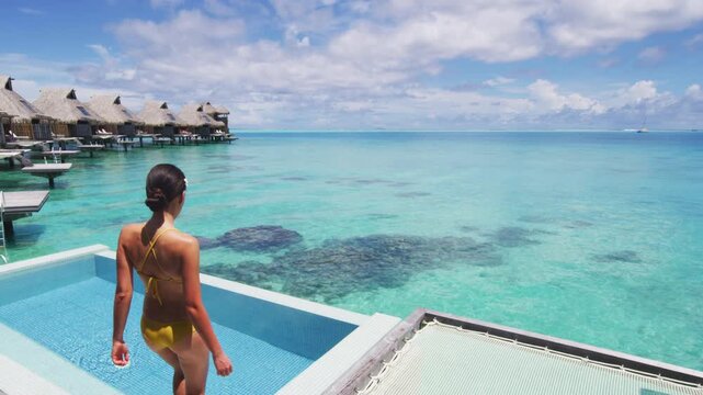 Luxury resort hotel woman walking on her private terrace deck of overwater bungalow with pool view on turquoise ocean - honeymoon suite. Raw vertical video of real woman model without makeup
