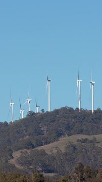 Wind Turbines Rotating on Grassy Hills Under Clear Blue Sky