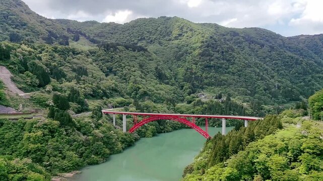 Aerial view of red bridge crossing emerald river in forested mountains