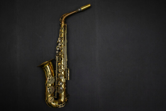 Golden alto saxophone on vintage dark leather background. Classic brass alto saxophone placed horizontally on a clean dark black textured leather background,